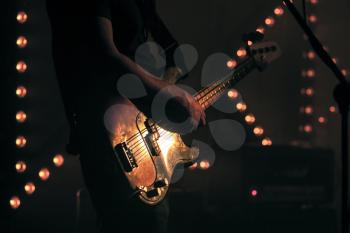 Electric bass guitar player on the stage with strobe illumination background, live hard rock music theme