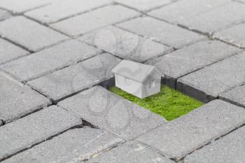 Gray cobblestone road pavement with missed block with fresh green grass and small white house model inside, mixed media with 3d rendering illustration