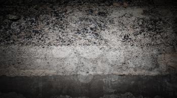 Grungy dark concrete wall with faded stucco layer and stones, closeup flat background photo texture