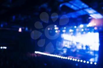 Blurred photo background, life music concert hall with blue illumination and crowd of people