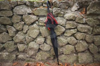 Black umbrella stands next to old stone wall in autumn park