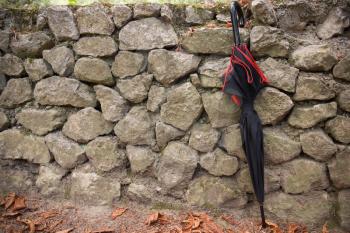 Black and red umbrella stands next to old stone wall in autumn park