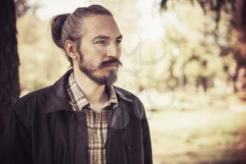 Outdoor portrait of young bearded serious man in summer park, vintage tonal correction filter effect