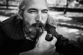 Bearded Asian man smokes a pipe, black and white face portrait with selective focus