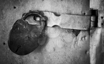 Old rusted lock hangs on metal door. Close-up black and white photo