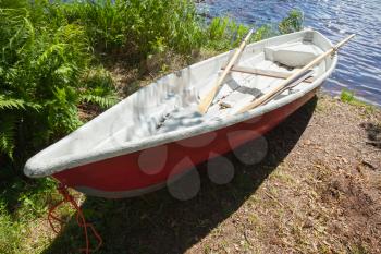 Small plastic red and white rowboat lays on coast of still lake