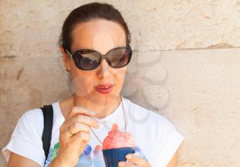 European young adult woman eats pink fruit ice cream, close-up outdoor portrait 