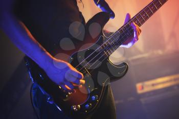 Electric bass guitar player on a stage, closeup photo with soft selective focus