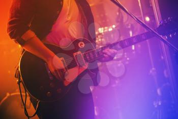 Electric guitar player plays on a stage with colorful scenic illumination, soft selective focus