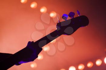 Electric bass guitar player over bright blurred stage lights, close-up silhouette photo with soft focus