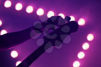 Live music background, guitarist tunes electric bass guitar, closeup photo with soft selective focus and purple illumination
