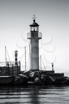 Lighthouse tower stands on the entrance breakwater in port of Burgas, Black Sea coast, Bulgaria. Vertical black and white photo