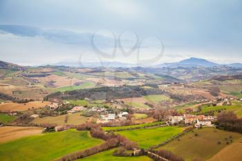 Rural panorama of Italian countryside in springtime. Province of Fermo, Italy. Villages and fields on hills under blue cloudy sky