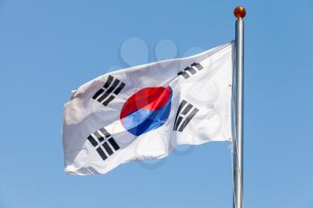 Flag of South Korea, also known as the Taegukgi waving on a flagpole over blue sky background