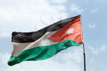Flag of Jordan waving on wind over cloudy blue sky in a sunny day