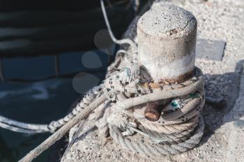 Mooring bollard with tied naval ropes stands on concrete pier in harbor, close-up photo