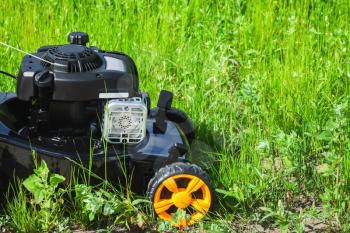 Grass mower stands on green lawn in summer garden, close-up photo
