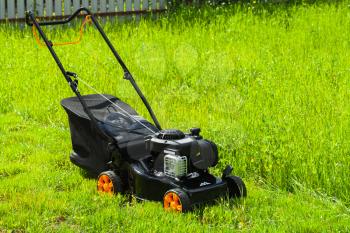 Modern gasoline powered grass mower stands on fresh green lawn in summer garden