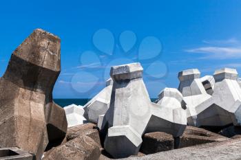Rough concrete breakwater blocks are under cloudy sky. Industrial background photo