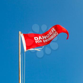 Danger for swimming. Red warning flag on a beach waving above blue sky. Close-up square photo