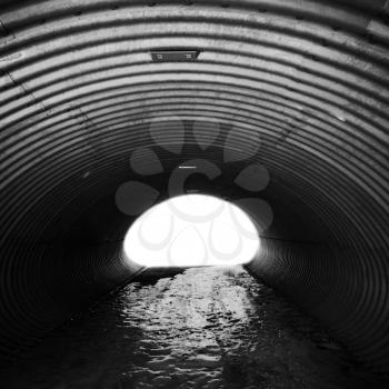 Corrugated steel corridor with glowing end and icy ground, industrial tunnel, square black and white background 