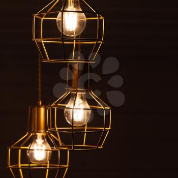 Ceiling chandelier with hanging three bulb lamps, yellow LED lighting elements covered with metal wire frame lampshades, square framed photo with selective focus