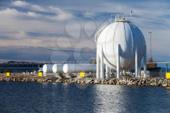 Modern white spherical gas holder stands on sea coast