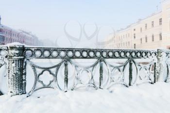 Forged green fence of Mogilev bridge covered with snow, Griboedov canal, Saint Petersburg, Russia