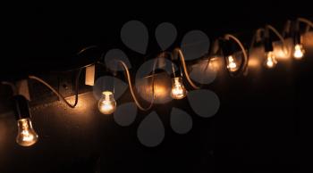 Vintage tungsten bulb lamps garland hanging on dark wall at night. Close up phtot with selective focus