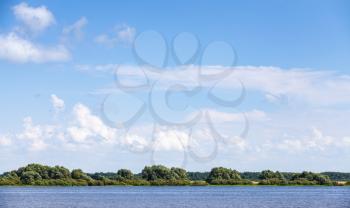Rural Russian landscape. Coast of Volkhov River under blue cloudy sky in summer day. Novgorod Oblast, Russia