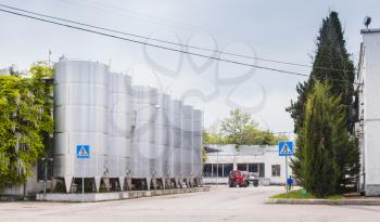 Shiny steel tanks stand in a row along empty street, modern wine factory equipment