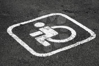 Place for disabled persons car on a parking lot, white road marking on dark asphalt. Close-up photo with selective focus