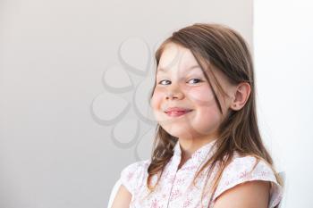 Smiling funny blond Caucasian little girl, close-up portrait over white wall background