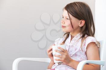Portrait of blond little girl with white cup of hot drink, close-up photo over white wall background