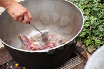 Cook mixes lamb pieces in cauldron. Preparing of Chorba soup on open fire, traditional meal for many national cuisines in Europe, Africa and Asia 