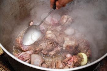 Mixing boiled lamb in cauldron. Preparing of Chorba soup on open fire, traditional meal for many national cuisines in Europe, Africa and Asia 