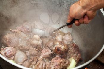 Mixing boiled lamb in a cauldron. Preparing of Chorba soup on open fire, traditional meal for many national cuisines in Europe, Africa and Asia 