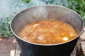 Broth with lamb and vegetables boil in a cauldron. Preparing of Chorba soup on open fire, traditional meal for many national cuisines in Europe, Africa and Asia 