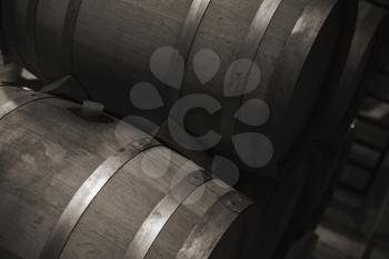 Wooden barrels with red wine in dark winery, monochrome photo with selective focus