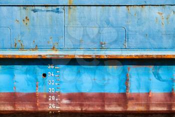 Blue cargo ship hull with red waterline and draft marks, front view, background texture