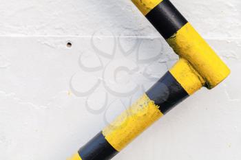 Metal railing with yellow black caution pattern over white wall background, abstract industrial object