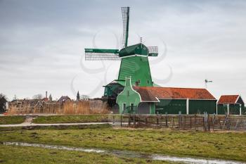 Old wooden Windmill near green barns on Zaan river coast, Zaanse Schans town, popular tourist attractions of the Netherlands. Suburb of Amsterdam