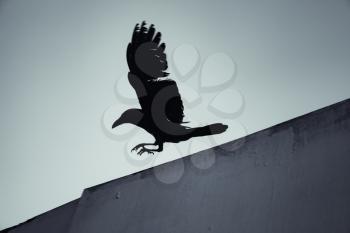 Black crow flying under blue sky, dark stylized silhouette photo with tonal filter effect