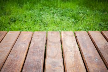 Perspective view of new wooden boardwalk over lawn with green grass, natural park background. Close-up photo with selective focus