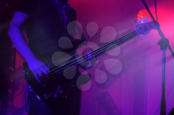 Electric bass guitar player on a stage in purple illumination, photo background with motion blur effect