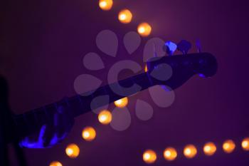 Electric bass guitar fragment over blurred stage lights, close-up silhouette photo with soft focus