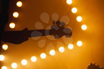 Live music background, bass guitar player over bright strobe stage lights, close-up silhouette photo with soft selective focus