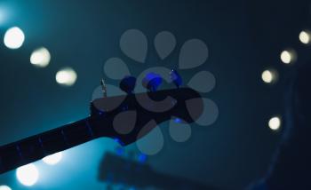 Live music background, electric bass guitar headstock silhouette in blue stage lights, close-up photo with soft selective focus