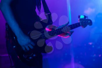 Live rock music background, bass guitar player on a stage, close-up photo with soft selective focus