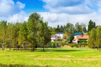 Rural Finnish landscape, trees and houses on hill near green meadow